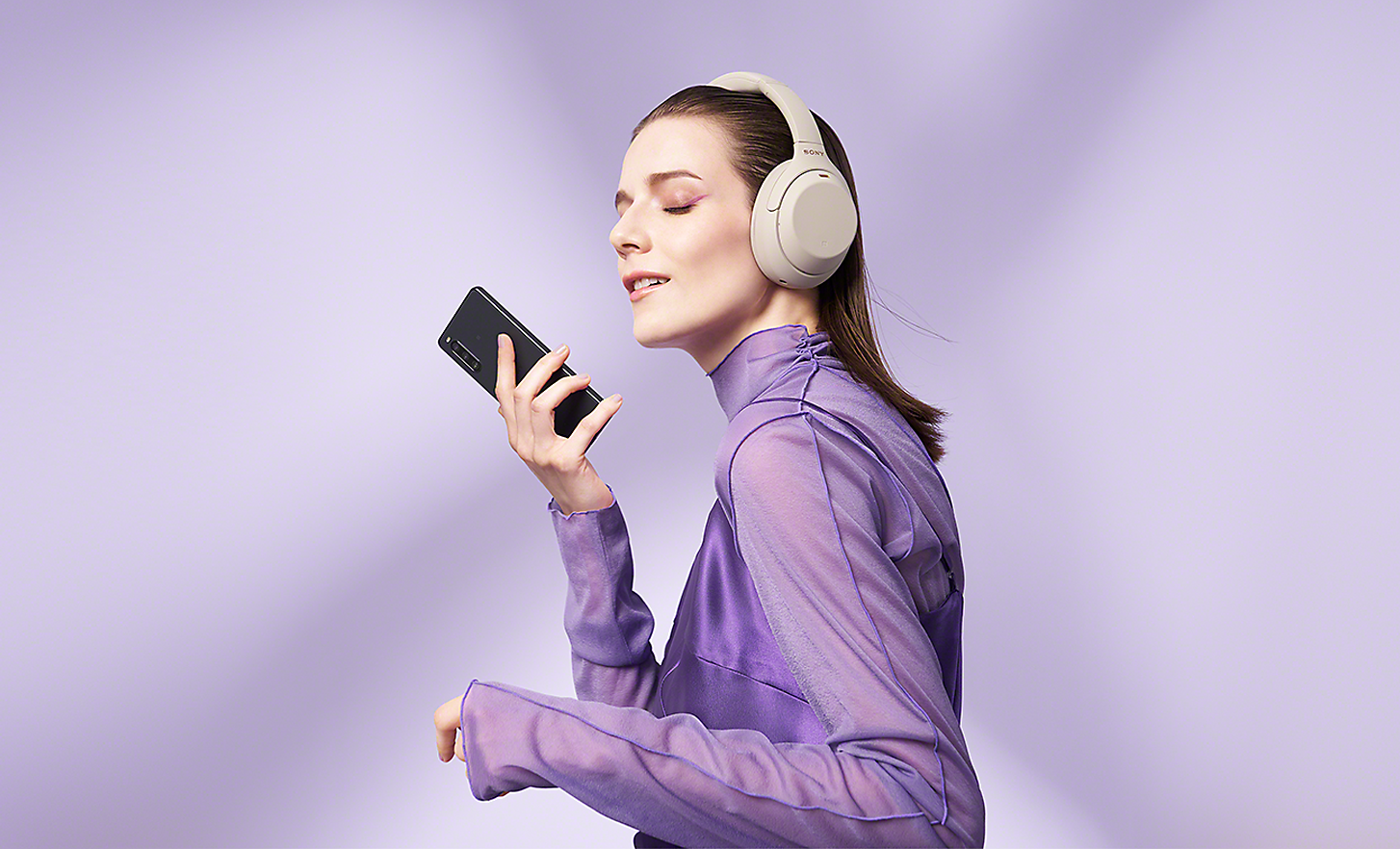 A woman wearing headphones and holding an Xperia 10 IV