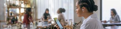 Image a person in a coffee shop using an Xperia phone and listening to a pair of Sony in-ear headphones