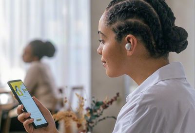 Image a person in a coffee shop using an Xperia phone and listening to a pair of Sony in-ear headphones