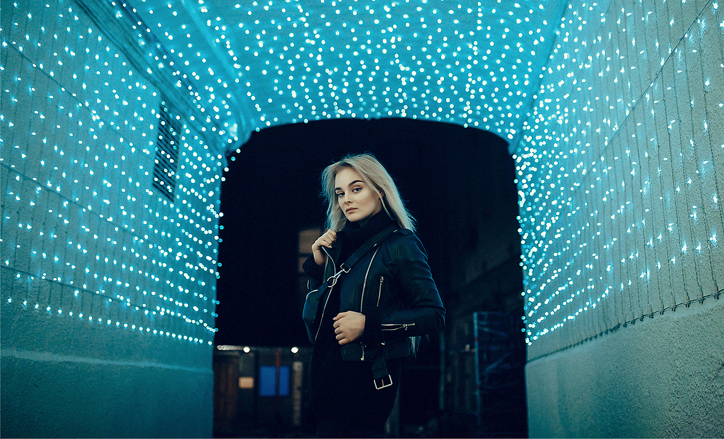 A night time portrait of a woman in a tunnel of fairy lights