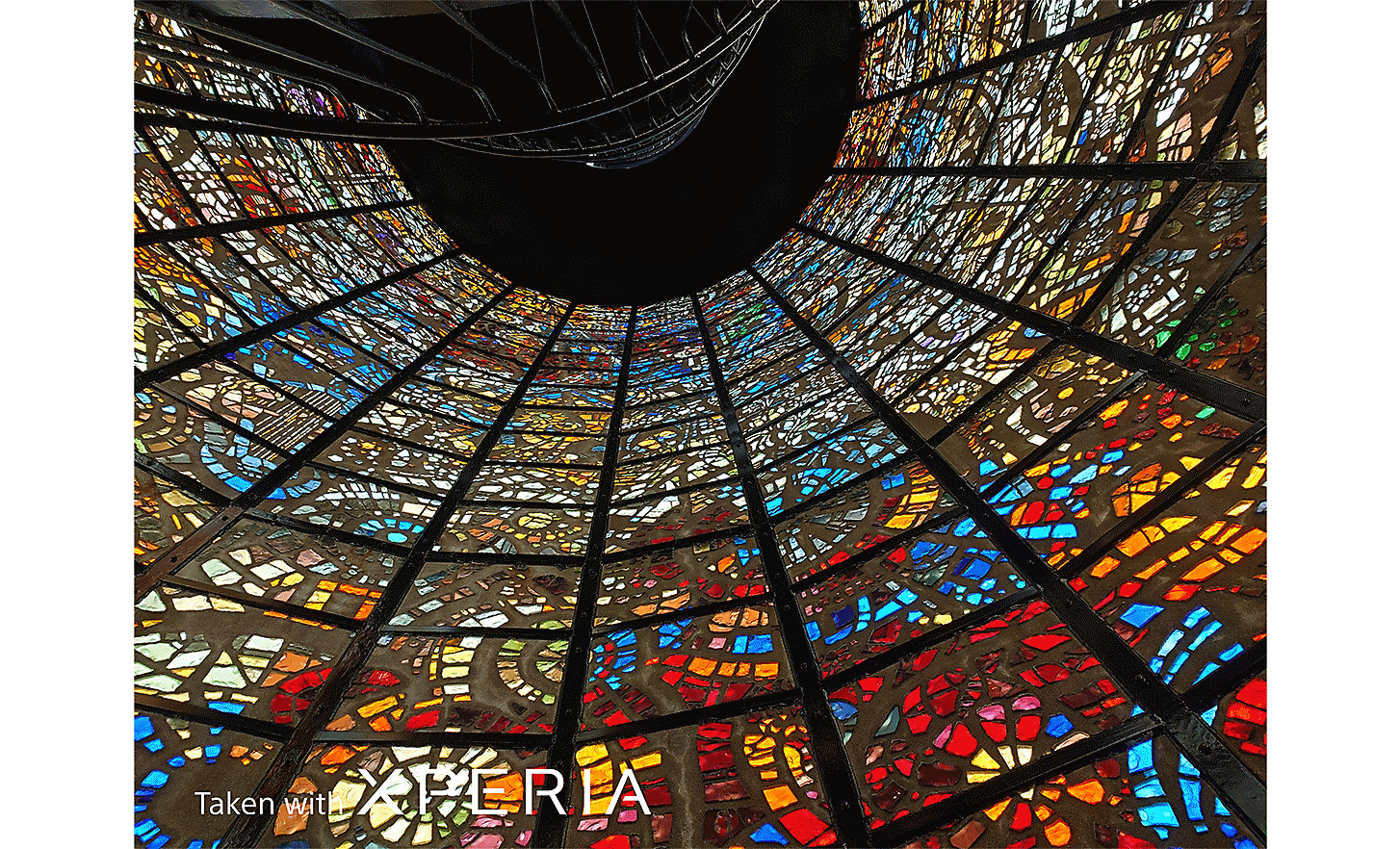 Dramatic image of a vast, brightly coloured, stained-glass window. Text reads "Taken with XPERIA".
