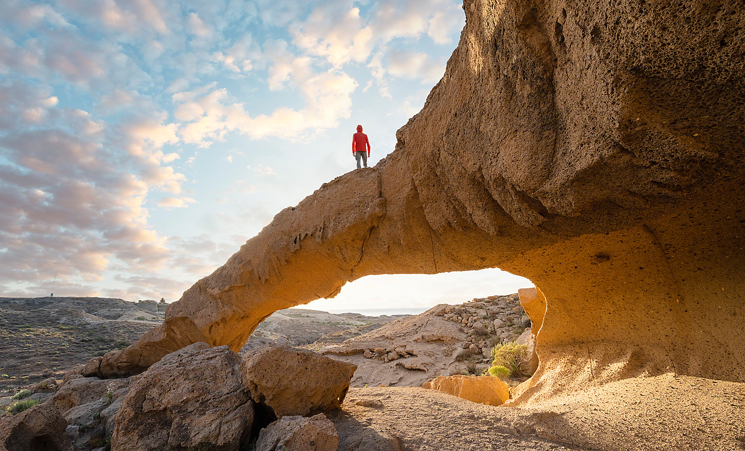 一位男士站在岩層上，眺望沙漠風景的超廣角相片