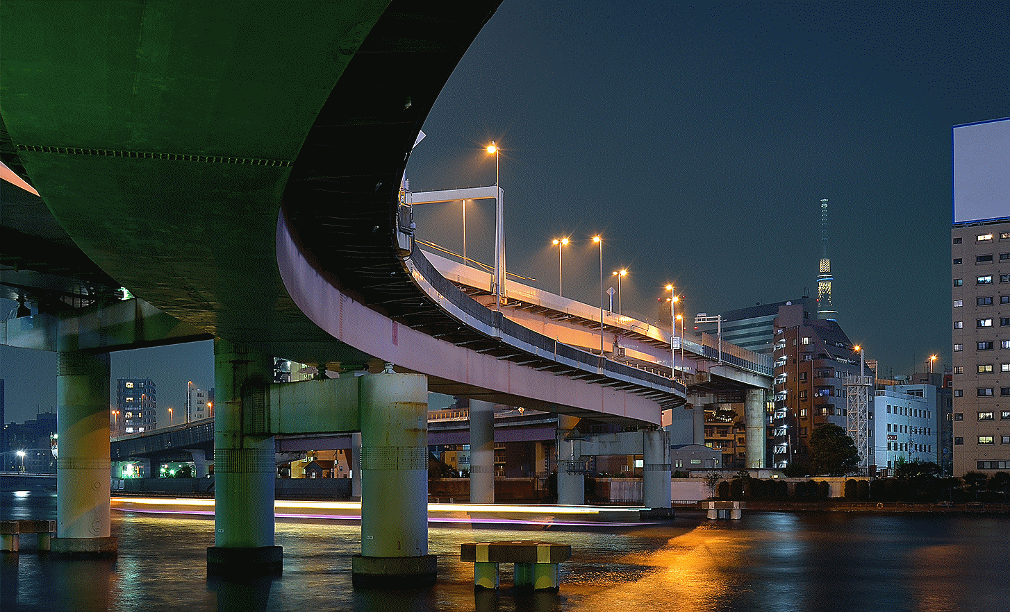 Obrázok vyvýšenej diaľnice v mestskom prostredí pri slabom svetle