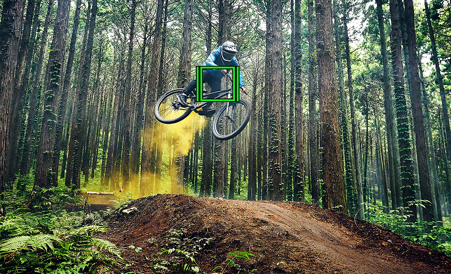 Người đi xe đạp leo núi đang cho xe nhảy trong một khu rừng với ô vuông màu xanh lá biểu thị tính năng Theo dõi trong thời gian thực