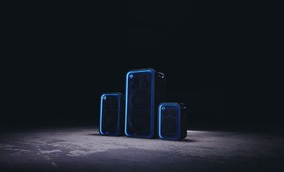 Fotografía de tres parlantes, el ULT TOWER MAX, el ULT TOWER 7 y el ULT TOWER 5, sobre un piso de concreto con un fondo oscuro. Los tres tienen iluminación LED azul alrededor de las rejillas frontales.