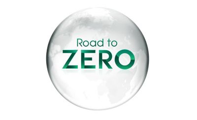 Un logotipo gráfico con el texto "Road to ZERO" centrado dentro de una esfera blanca translúcida y brillante que ilustra un mapa gris tenue de los continentes. Las palabras "Road to" están escritas en una tipografía verde delgada, justo encima de la palabra "ZERO", la cual aparece en una tipografía verde llamativa, gruesa y de estilo geométrico con un sutil sombreado degradado