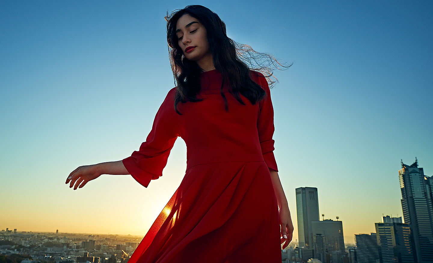 Retrato con poca luz de una mujer con un vestido rojo con un paisaje urbano de fondo