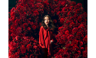 紅色花朵簇擁著一位身穿紅衣的女士（85 毫米微距拍攝）