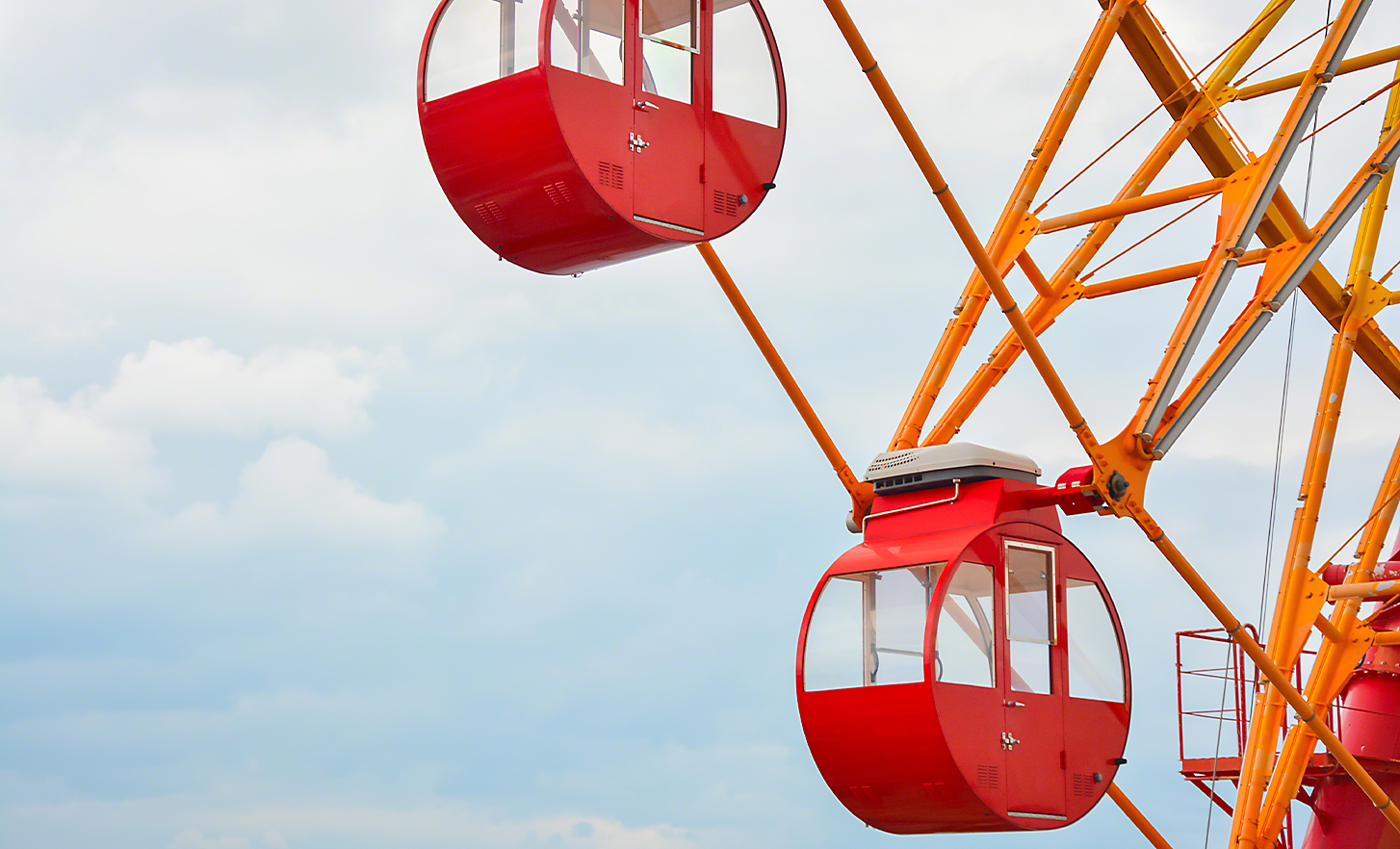 A bright orange and red big wheel against a cloudy sky