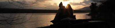 Image of two people sitting close to each other, with an evening scene in background