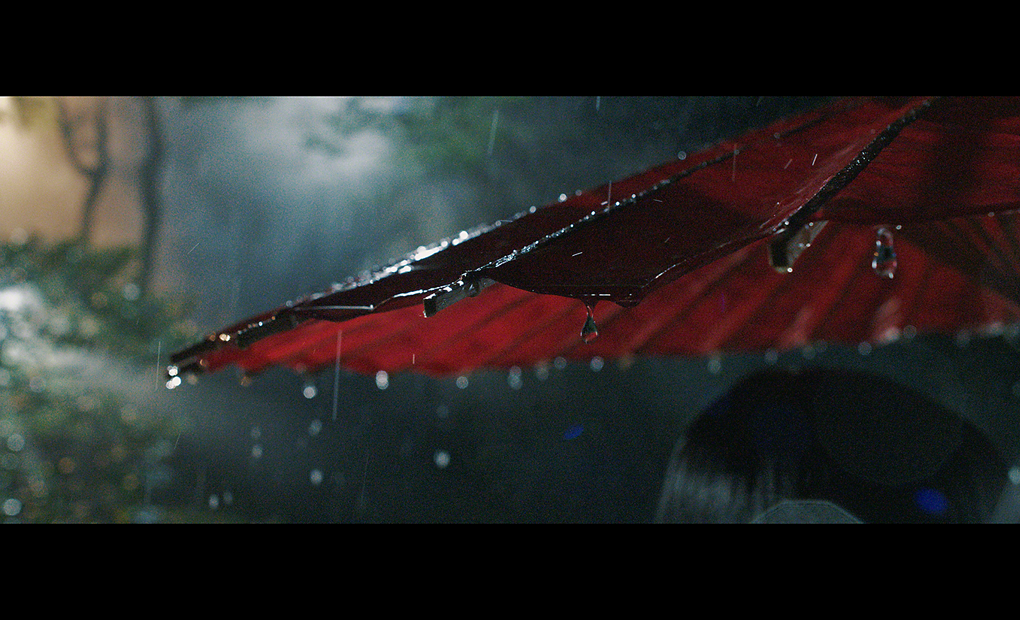 Snímek deště skapávajícího z červeného slunečníku pořízený za slabého osvětlení