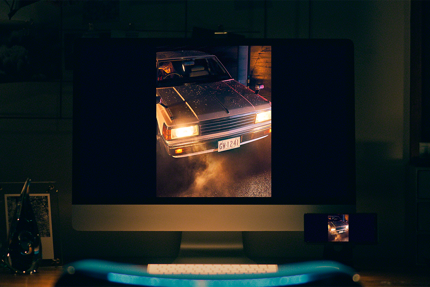 Stolní počítač se snímkem automobilu s rozsvícenými předními světly pořízeným za slabého osvětlení