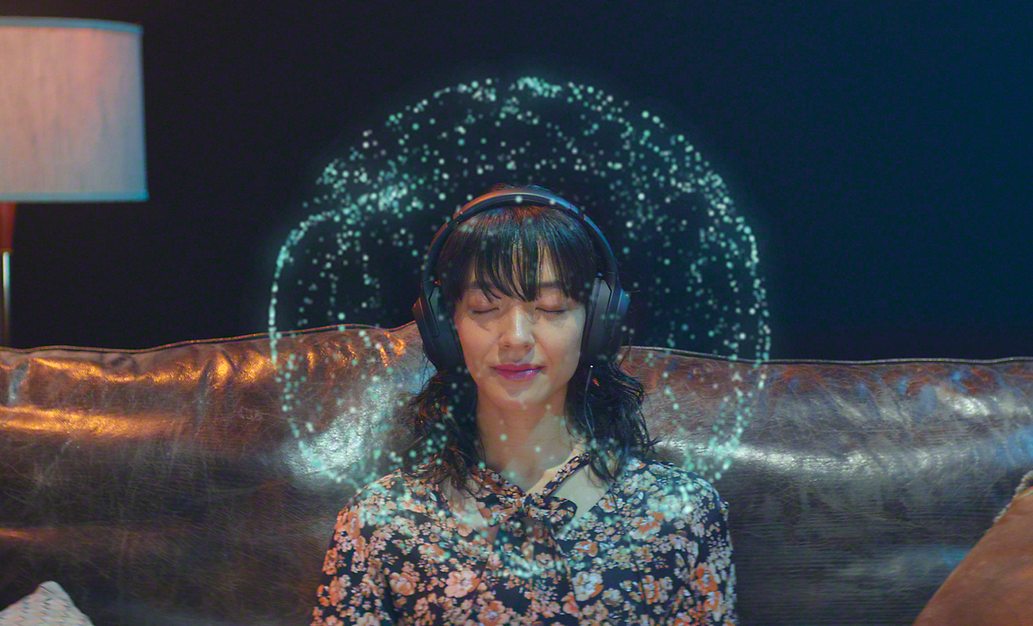 Una mujer con los ojos cerrados escuchando música de los altavoces. Los puntos de luz alrededor de su cabeza representan 360 Reality Audio