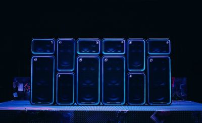 Varios parlantes para fiestas de Sony, incluidos los ULT TOWER 5, ULT TOWER 7 y ULT TOWER MAX, están apilados en posición vertical y horizontal y forman una gran pared de parlantes en un escenario. El contorno de la rejilla rectangular frontal de cada unidad está delineado por una llamativa tira de luces LED azules y moradas, que crea un efecto de iluminación sincronizado. Los botones circulares "ULT" se iluminan con intensidad en toda la escena sobre un fondo completamente negro.