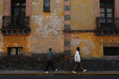 Image of two people walking past a building with a patterned brick wall in NT (Neutral) mode.