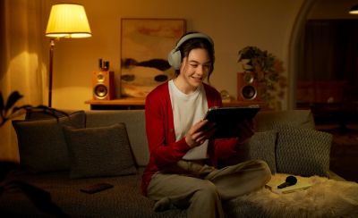 Photo of a person sitting on a sofa holding a tablet, with an ECM-AX10 microphone resting on a notebook beside them.