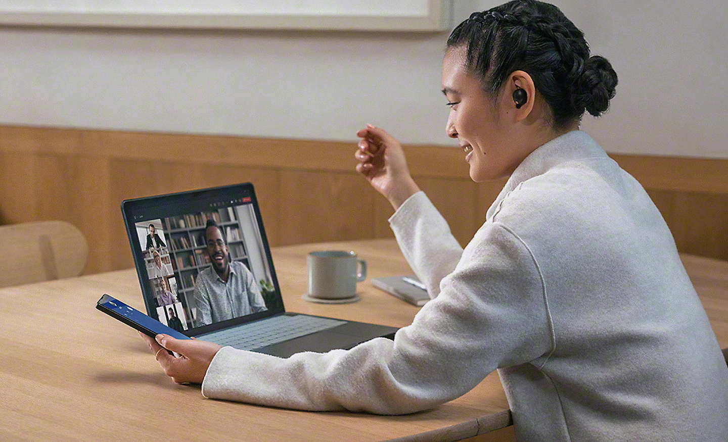En person har et møte på en bærbar datamaskin og bruker et par øretelefoner fra Sony med en Xperia-telefon i hånda