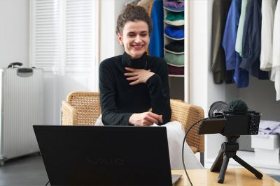 Una mujer realizando una transmisión en vivo frente a una laptop y una cámara situada sobre un trípode