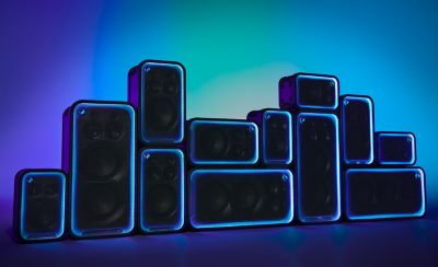 Una pared dinámica formada por los parlantes ULT POWER SOUND apilados en diferentes orientaciones verticales y horizontales. El contorno de cada unidad está delineado por brillantes anillos de luz LED azul neón sobre un fondo degradado azul y verde azulado.