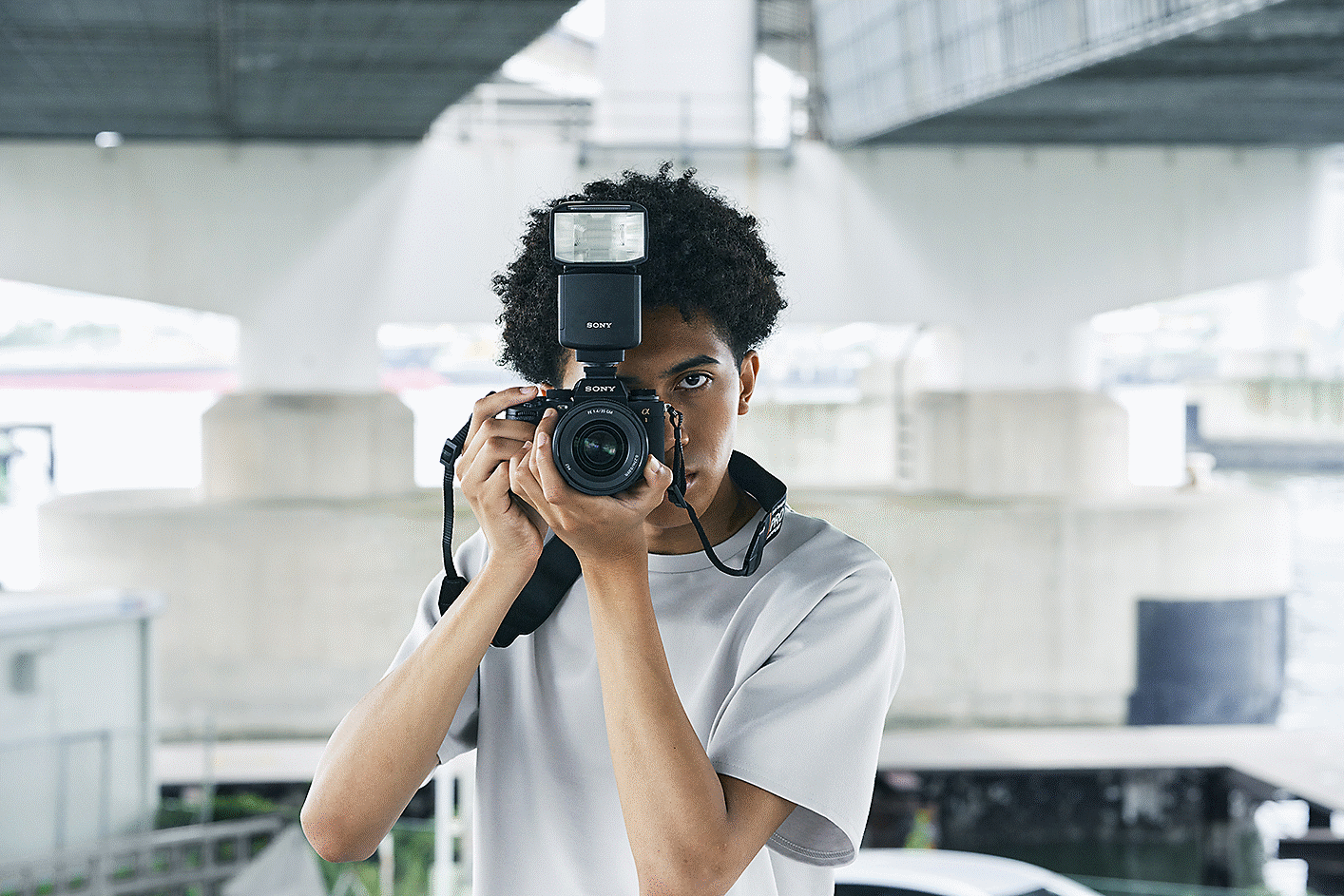 Posnetek moškega s fotoaparatom v rokah z bliskavico pred njim in mestom v ozadju