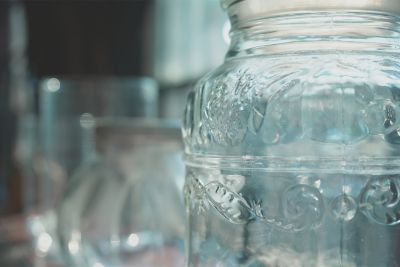 Close-up image of a transparent bottle with various shapes of cups in background bokeh in SH (Soft Highkey) mode