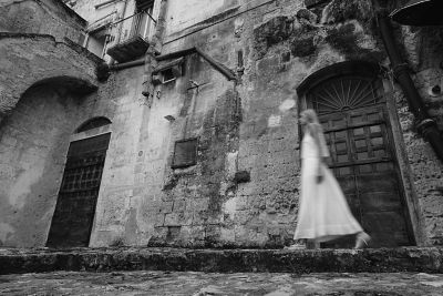 Image of a woman walking past a stone building in BW (Black & White) mode.