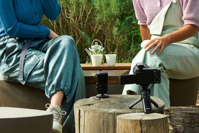 Image montrant deux personnes assises à l'extérieur avec un microphone devant elles et un appareil photo à proximité sur lequel est fixé un récepteur