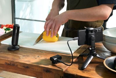 Image montrant une personne en train de cuisiner, avec le microphone à proximité, et le récepteur connecté à un smartphone sur un support via un câble USB