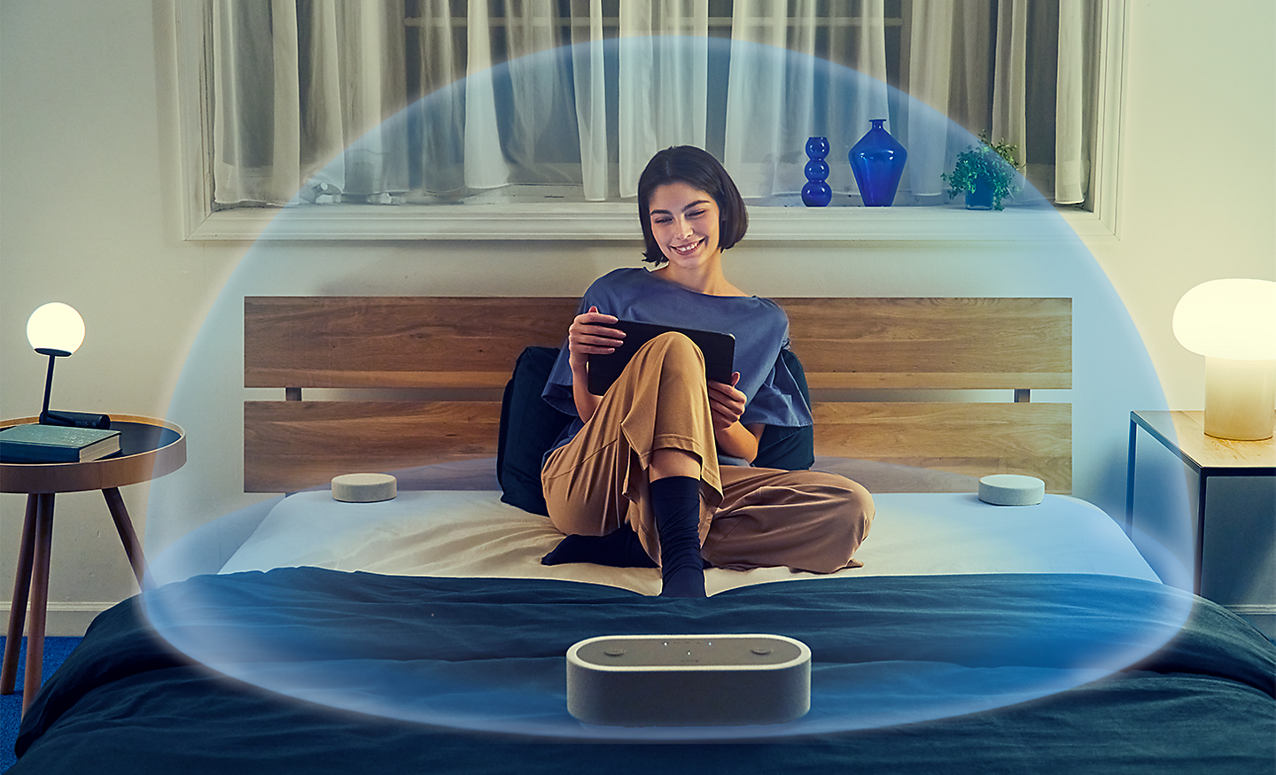 Image of a person sitting on a bed surrounded by the HT-AX7 and a transparent bubble encapsulating them with spatial sound