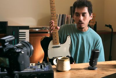 Image montrant un homme tenant une guitare et parlant dans le microphone à proximité, tout en regardant l'appareil photo sur lequel est fixé un récepteur