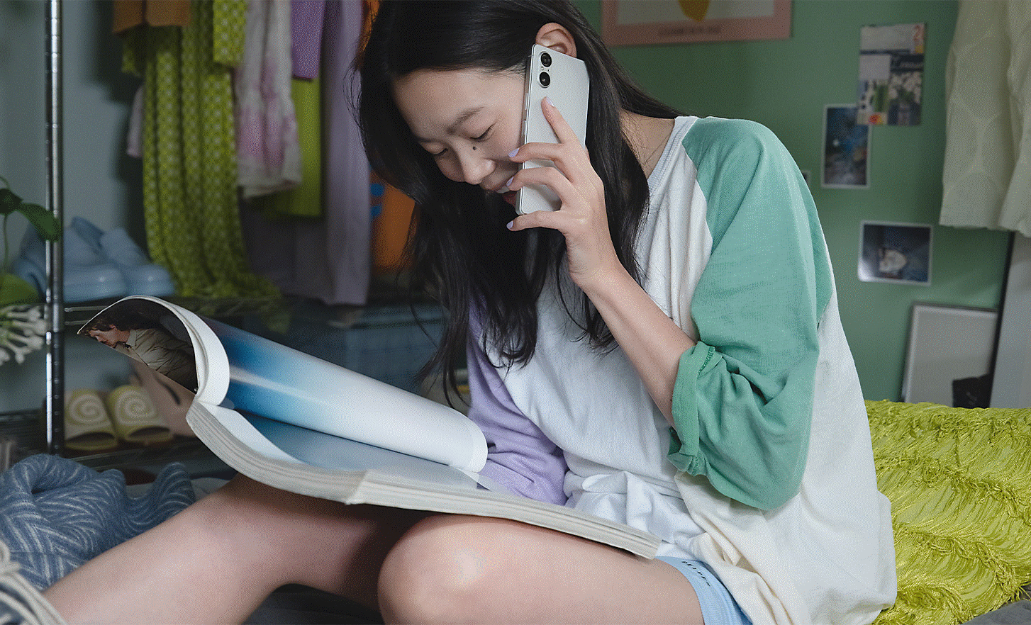 Image of a person talking on a silver Xperia 5 V whilst reading a brochure in a bedroom