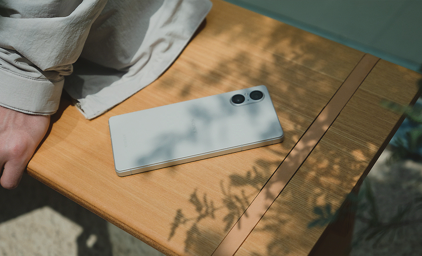 Close up image of a silver Xperia 5 V lying on a bench with a person sitting next to it