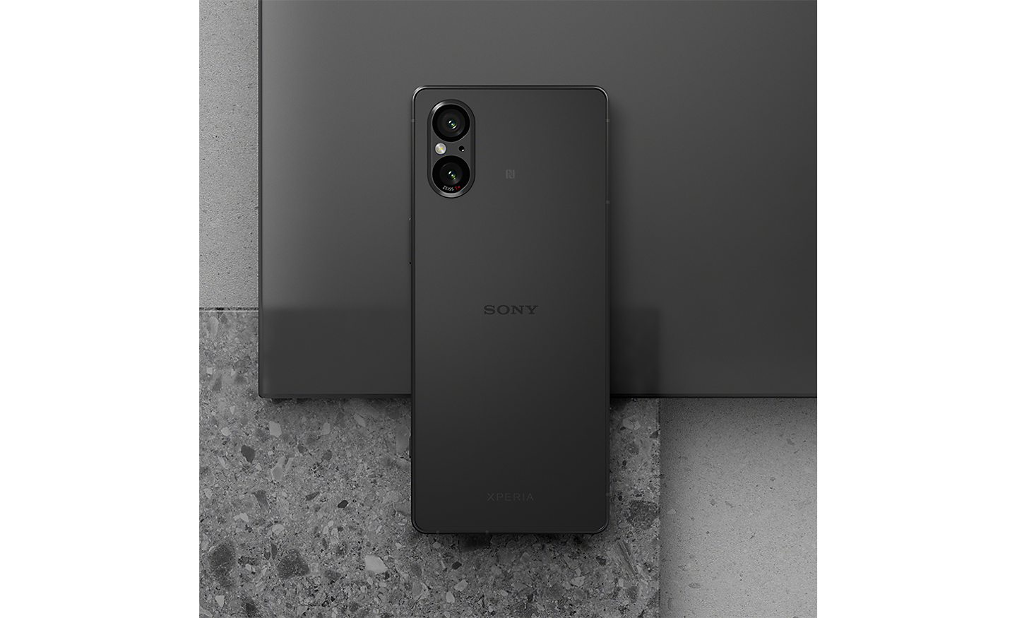 Image of a black Xperia 5 V sitting on a sheet of black plastic and grey granite