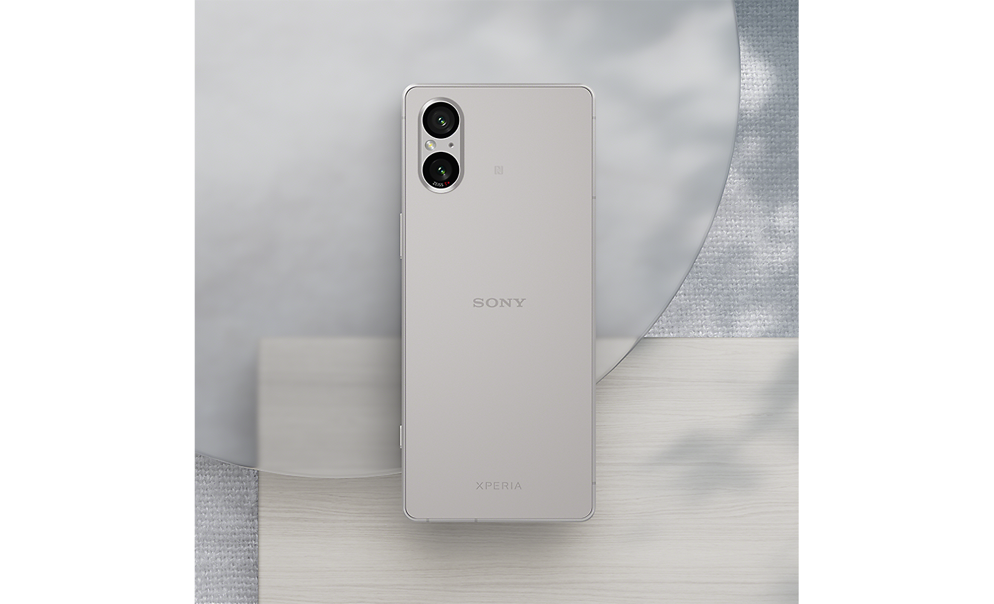 Image of a silver Xperia 5 V sitting on a variety of natural grey materials