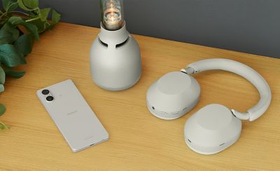 Изображение серебристого Xperia 5 V рядом с парой наушников Sony и лампой на столе.