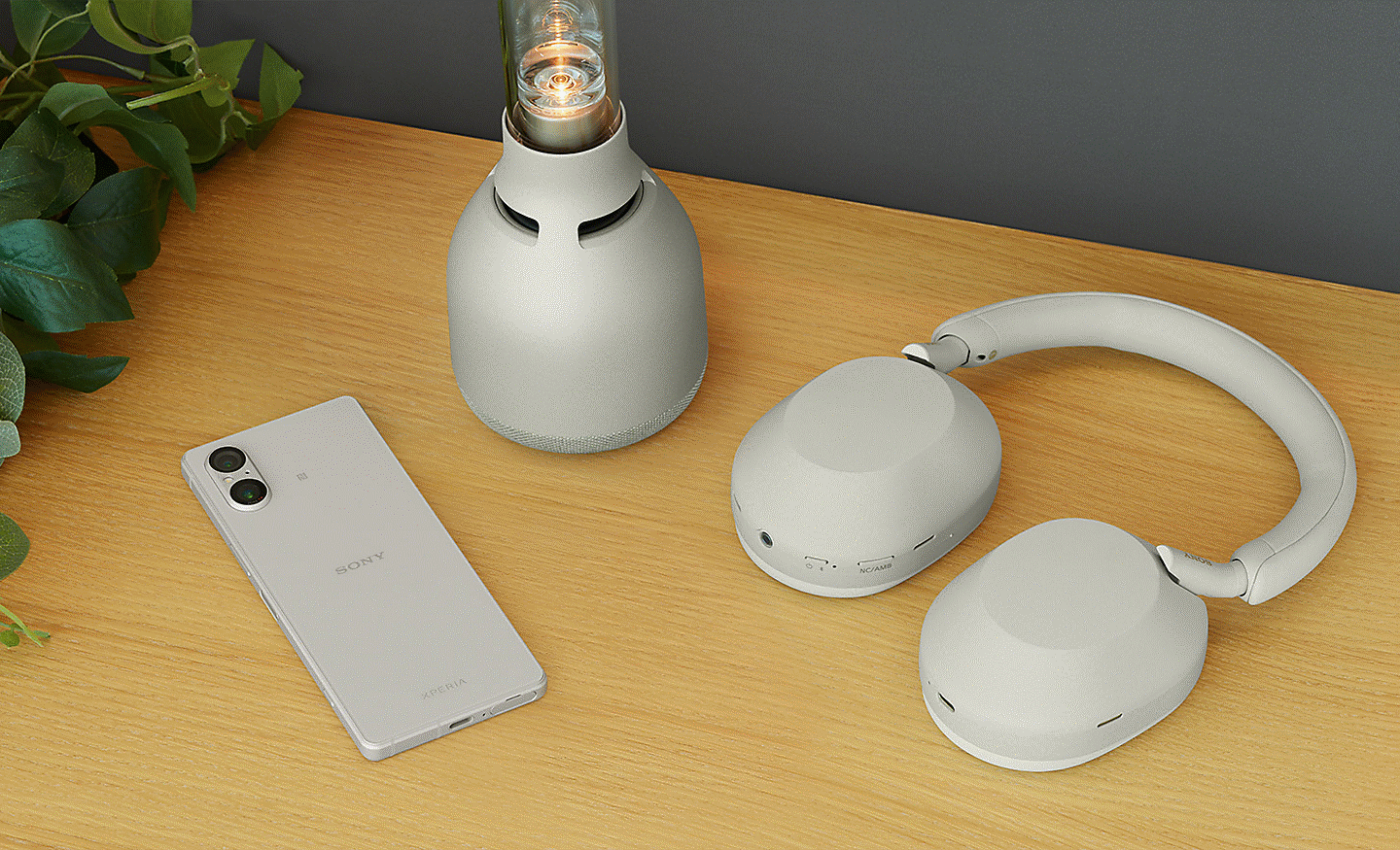Image of a silver Xperia 5 V sitting next to a pair of Sony headphones and a lamp on a desk