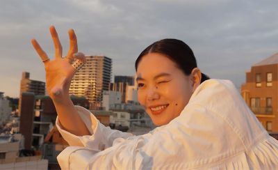 Image of a person on a rooftop holding their hand up to the sun with one eye closed