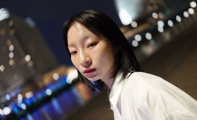 以一定角度拍攝的夜間人物特寫圖片，背景為模糊的城市景色