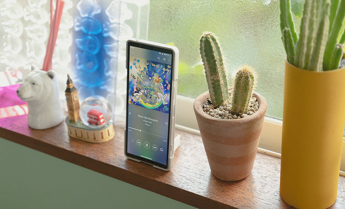 Image of an Xperia 5 V standing on a shelf, propped up by its stand, with a cactus and snow globe