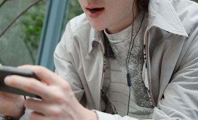 一個人在 Xperia 5 V 上玩遊戲的特寫圖片，對焦拍攝有線耳機上的麥克風元件