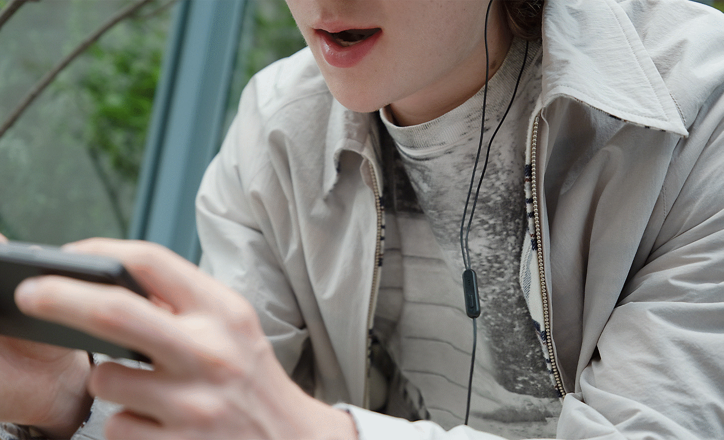 Close up image of a person playing a game on their Xperia 5 V focusing on the mic component on a pair of wired headphones