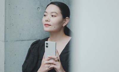 圖片展示一個人拿著銀色 Xperia 5 V 站在石屎牆旁