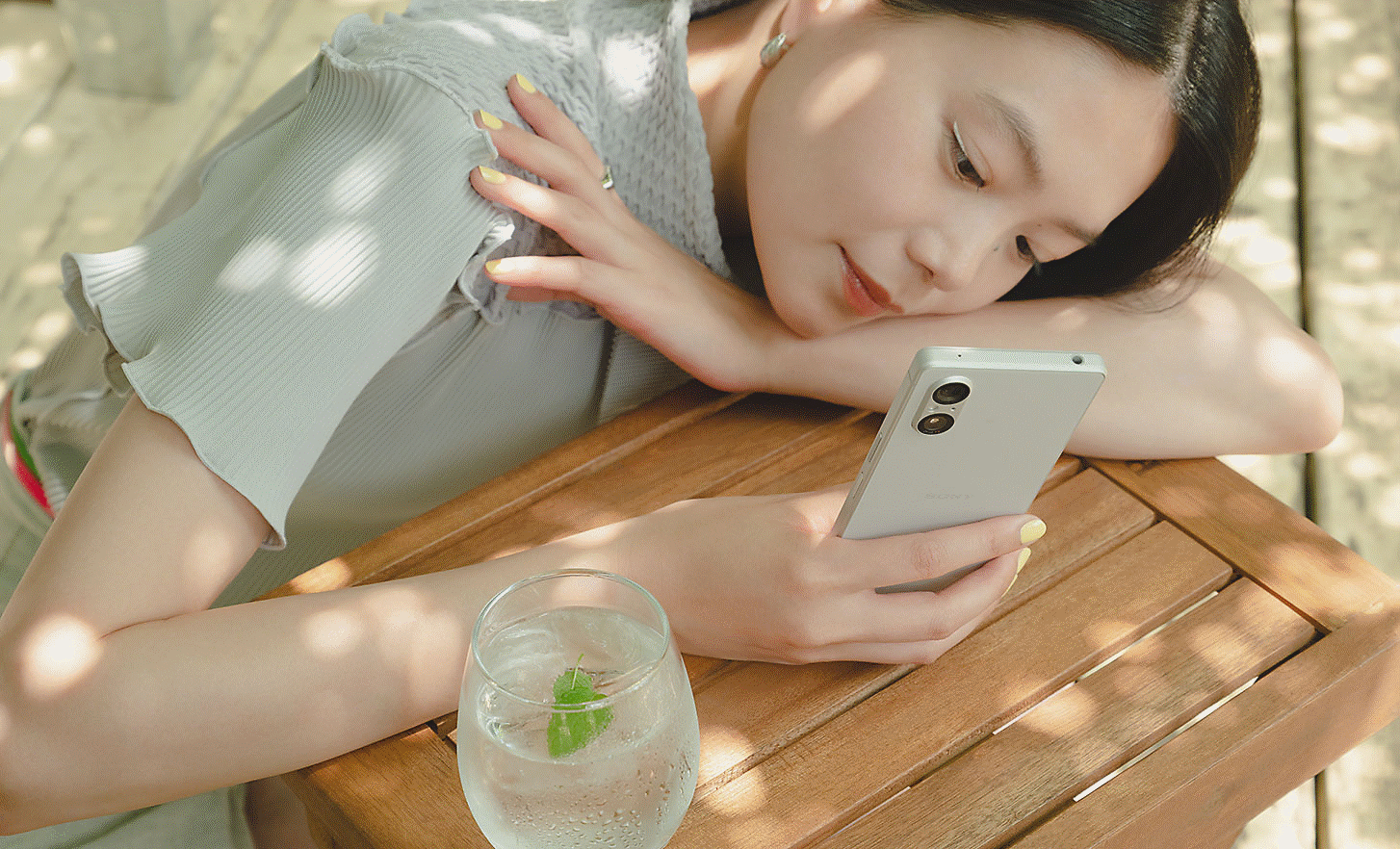 Image d'une personne penchée sur une table en bois avec un verre, en train d'utiliser un Xperia 5 V