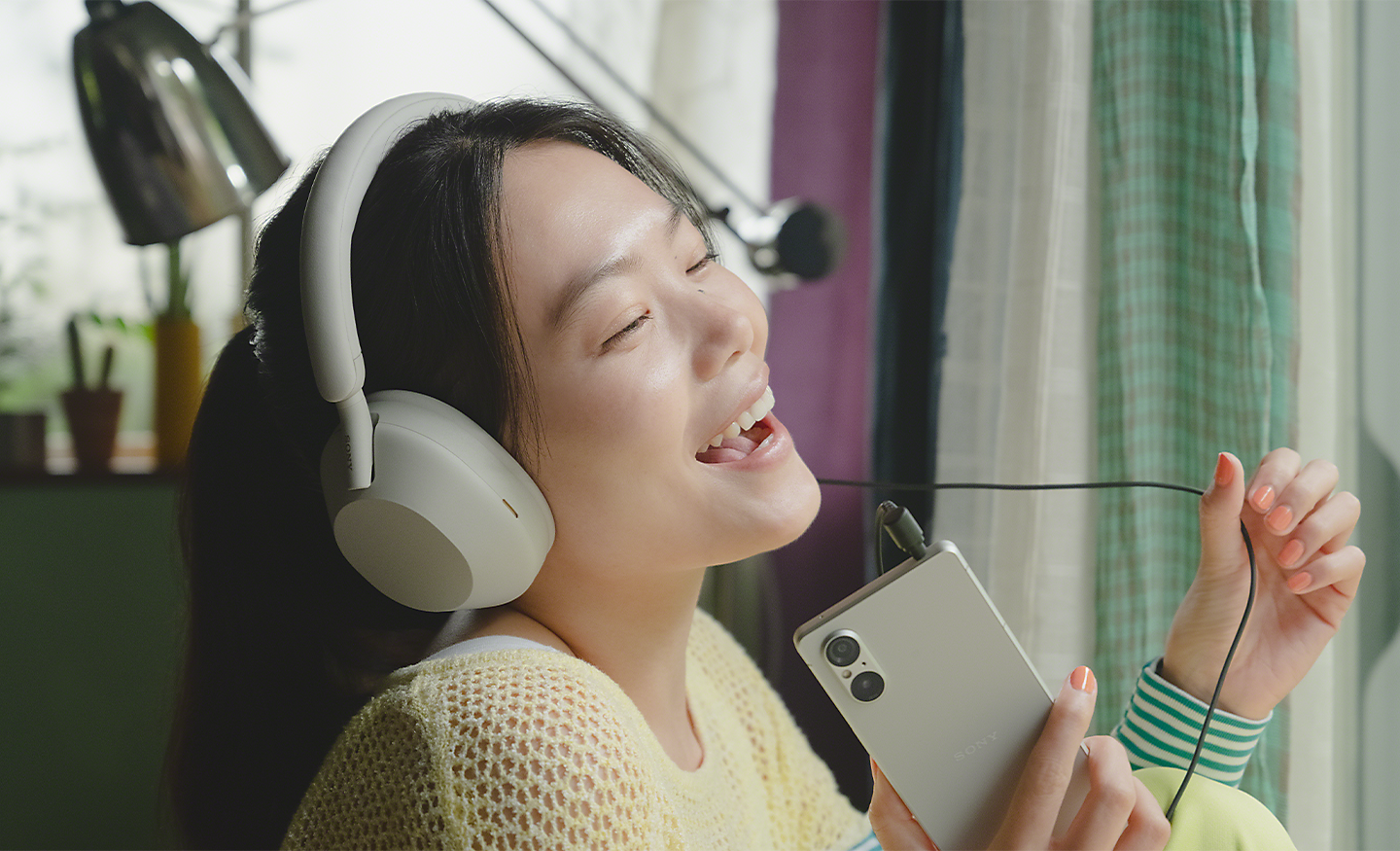Kép egy személyről, aki Xperia 5 V telefonon hallgat zenét fehér fejhallgatóval, és énekel a zenére