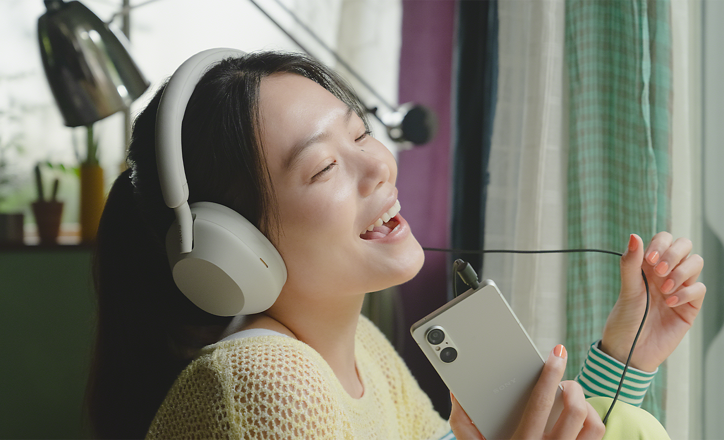 Image of a person listening to an Xperia 5 V with white headphones on and singing along to the music