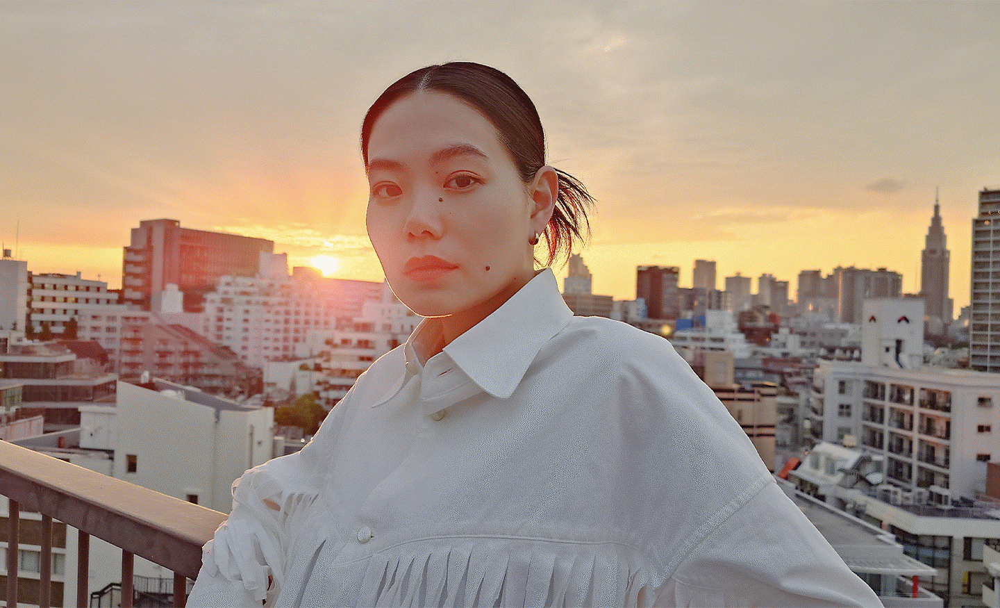 Image of a person on a rooftop with a sun setting over a city skyline in the background