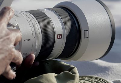 Product image showing close-up of user’s hands operating camera with telephoto lens mounted