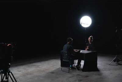 Image of two men talking face to face in a room with one light