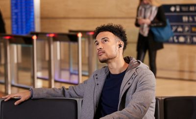 Мужчина в наушниках WF-1000XM4 ждет на лавочке на остановке