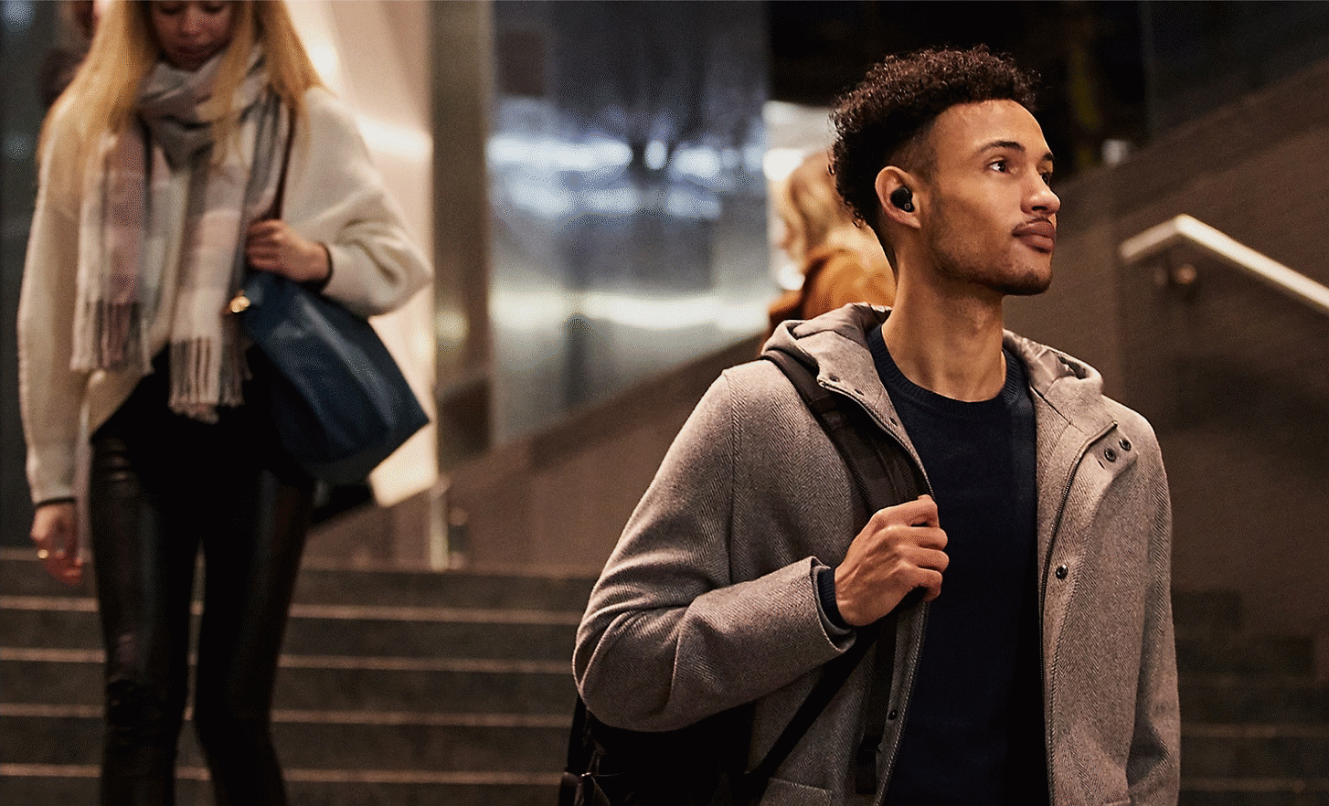 Man wearing WF-1000XM4 headphones, in a city at night, walking down steps